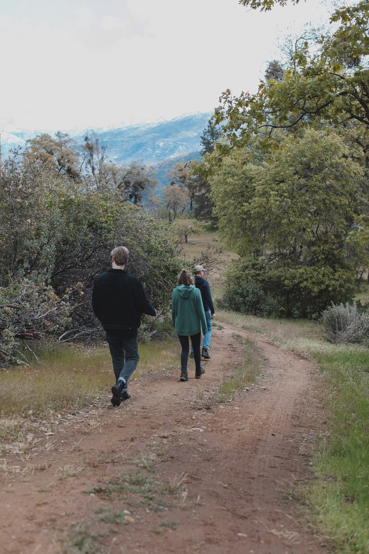 Three people walking a dirt trail toward the mountains
